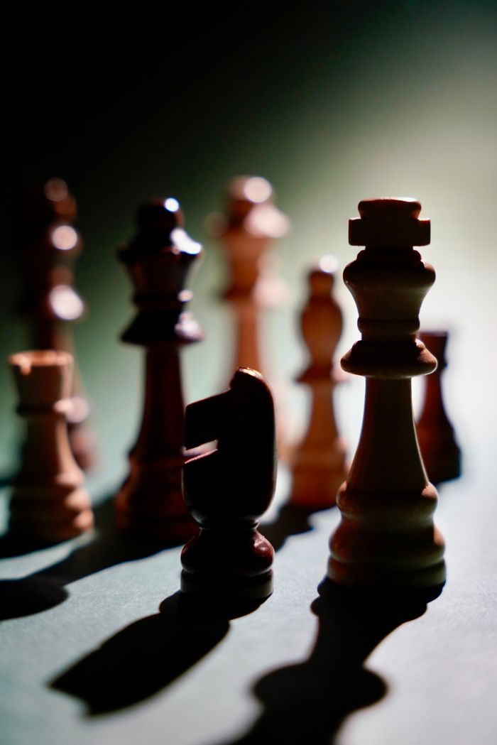 about-02 Chess pieces casting dramatic shadows on a chessboard, showcasing intense lighting and focus.