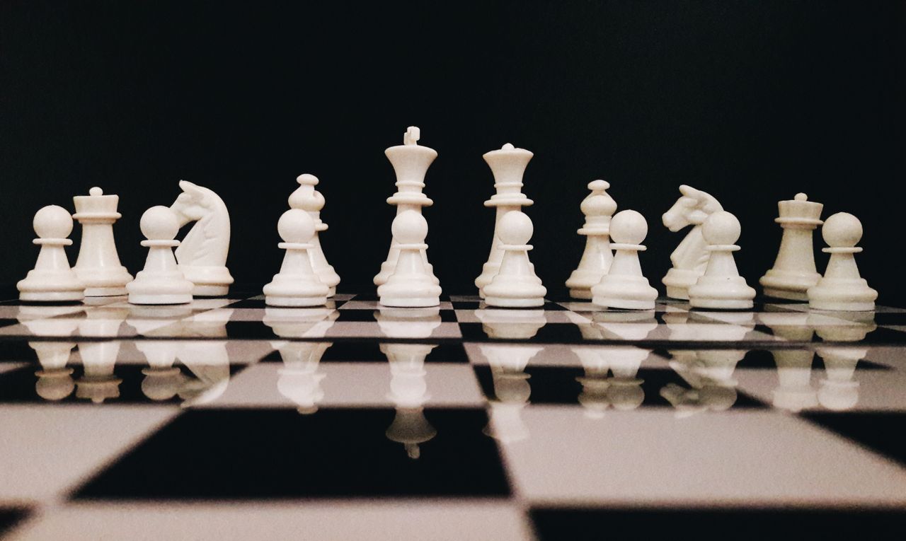 services-02 White chess pieces strategically placed on a board reflecting against a black background.